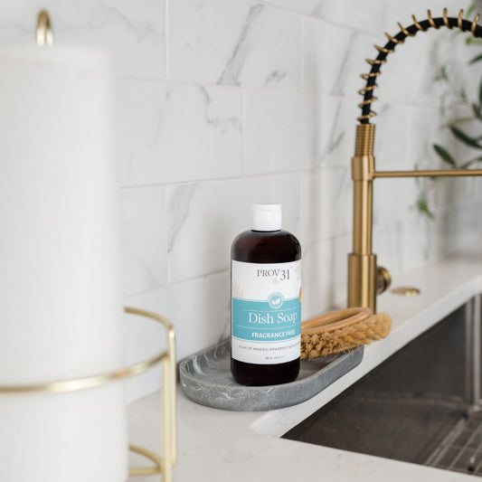 Bottle of PROV 31 dish soap on a marble kitchen counter by a sink with a gold faucet.