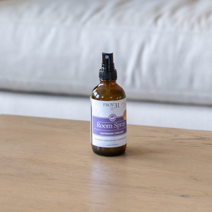 An amber glass spray bottle with a purple and white label that reads "PROV 31 Room Spray: Lavender Dreams" sits on a wooden coffee table.
