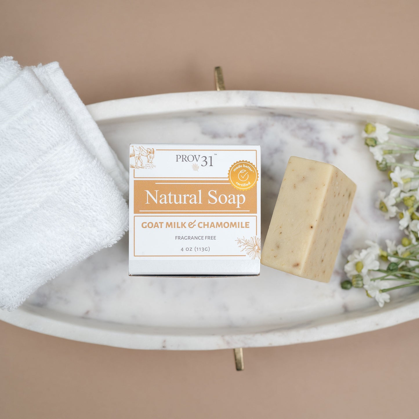 A bar of PROV 31 natural soap and its packaging box, styled on a white marble tray with a folded white towel and chamomile flowers against a solid beige background.