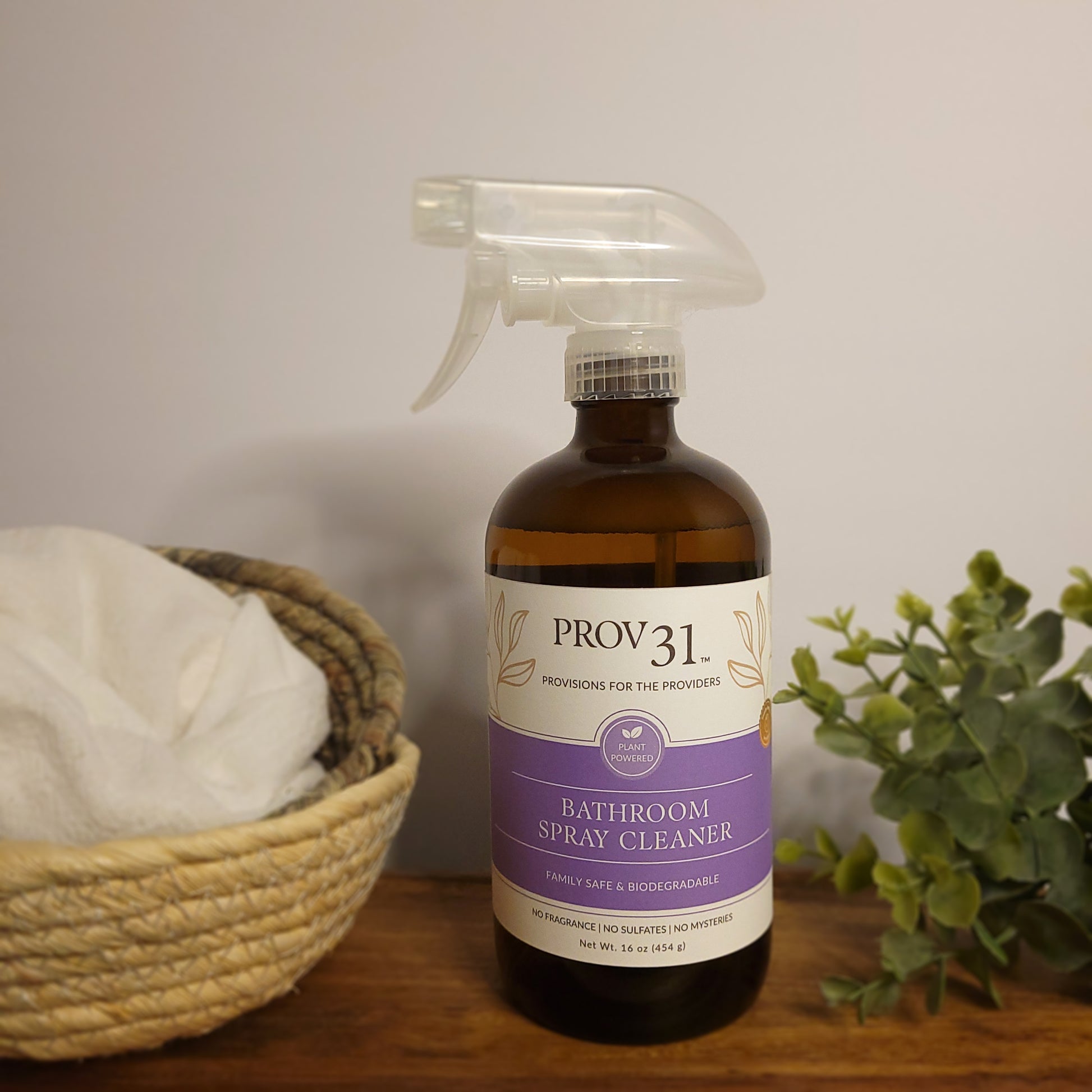 Bottle of Prov 31 Bathroom Spray Cleaner on a wooden surface with a basket and plant in the background.