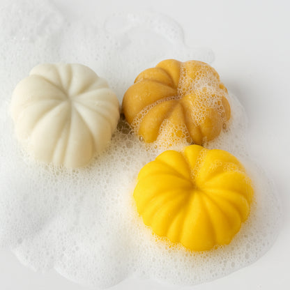 Three white, yellow, and orange bar soaps shaped like pumpkins with bubbles on a white background.