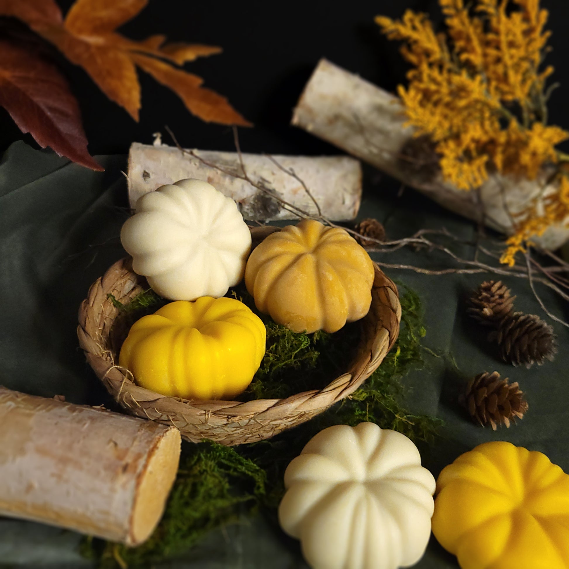 Decorative arrangement with pumpkin soaps in a basket, surrounded by autumn elements on a dark background.