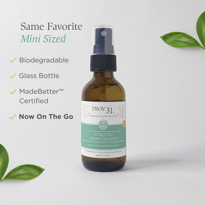 Glass bottle of Prov 31 Everyday Spray Cleaner with green leaves on a light gray background