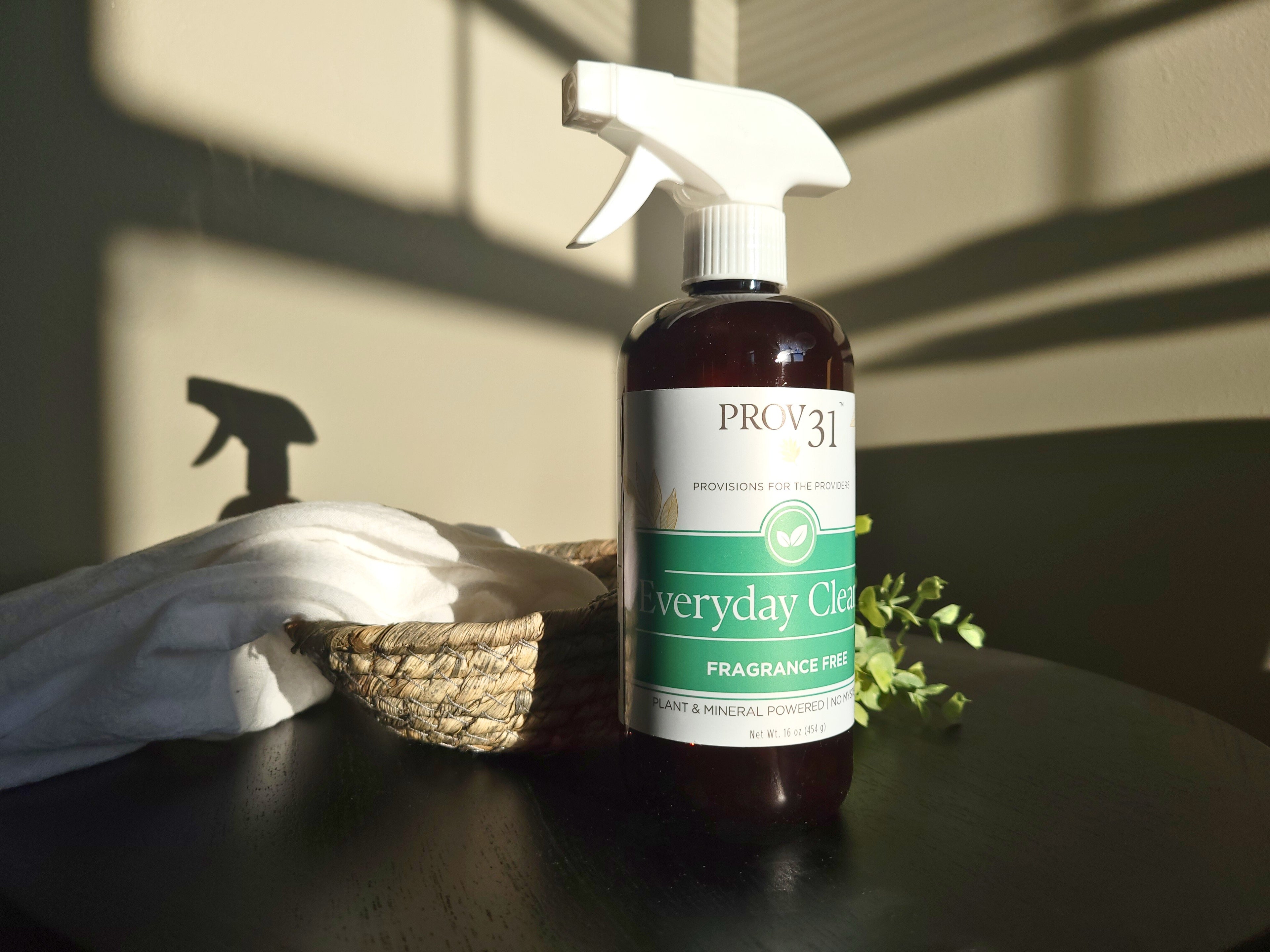 Bottle of Prov31 Everyday All Purpose fragrance-free cleaning spray on a table with a cloth and basket in the background.