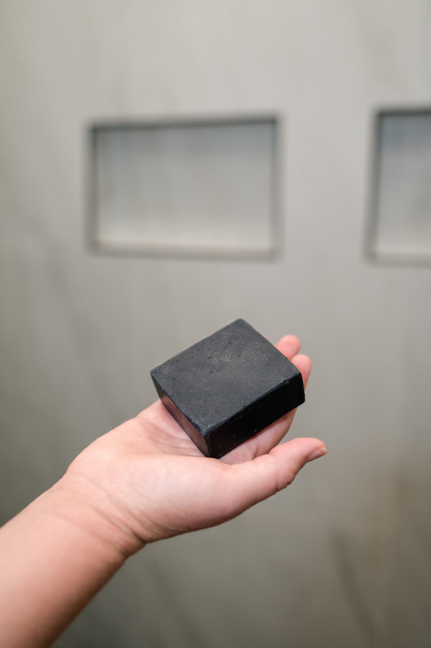 A hand holding a bar of PROV 31 natural charcoal soap in a shower.