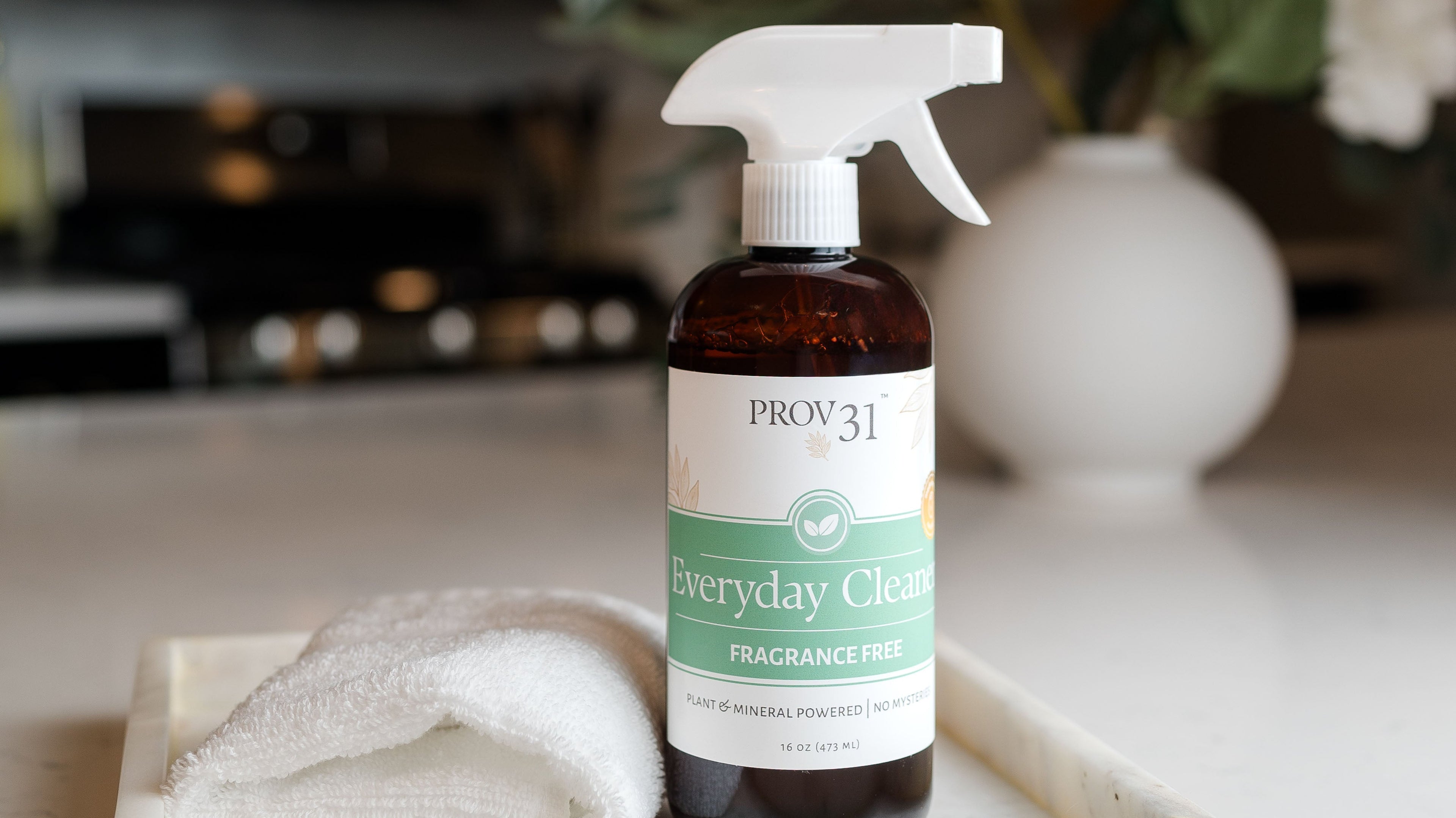 A bottle of PROV 31 Everyday Cleaner spray with a white trigger sprayer and a white label, placed on a white marble tray next to a folded white towel in a bright kitchen setting.