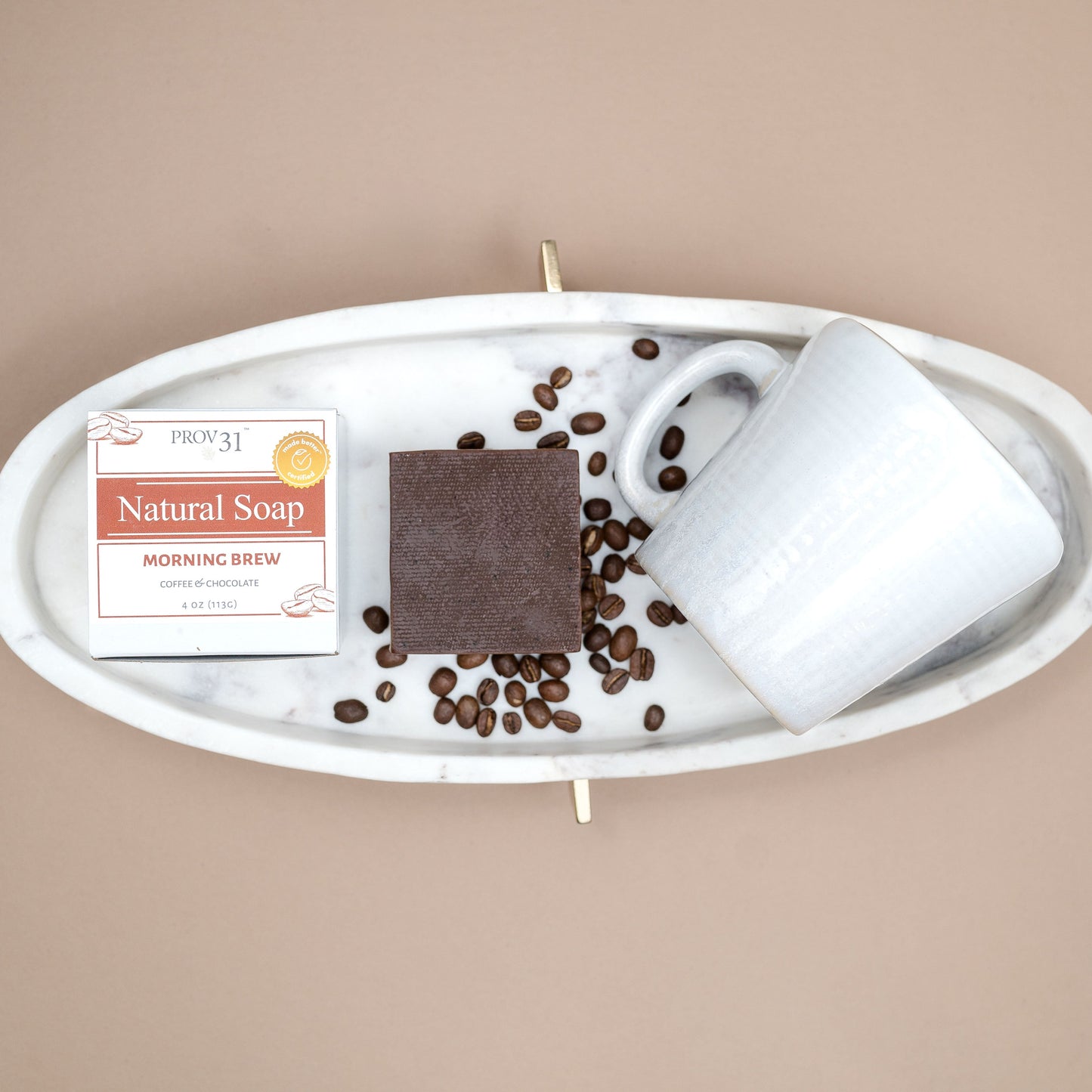 A styled flat-lay of a bar of PROV 31 natural soap in its packaging next to a white ceramic mug and scattered coffee beans on a white marble tray, set against a solid beige background.
