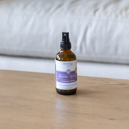 An amber glass spray bottle with a purple and white label that reads "PROV 31 Room Spray: Lavender Dreams" sits on a wooden coffee table.